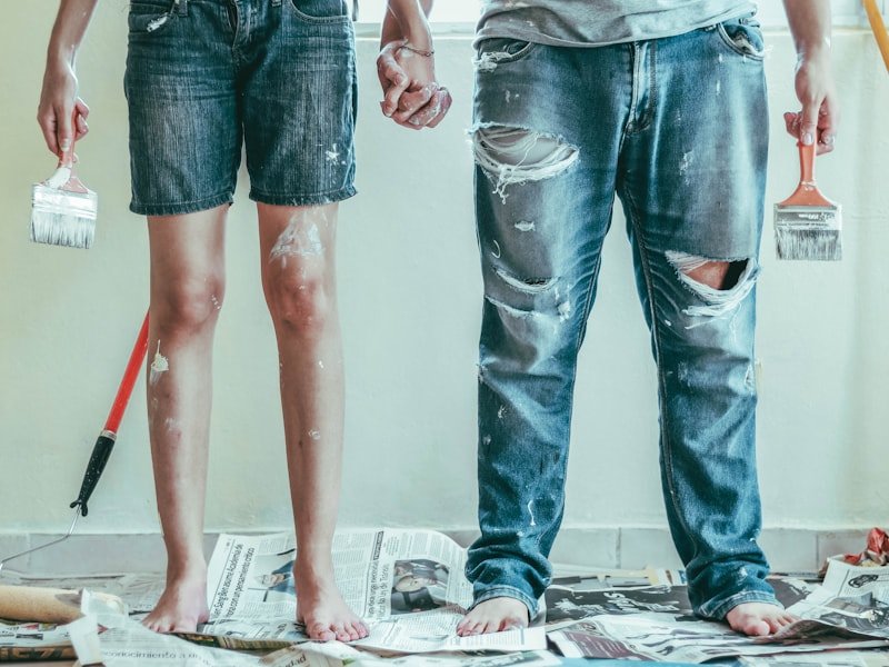 Paint-splattered jeans with brushes during an interior repaint.